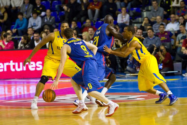 A player dribbling the ball up the court against multiple defenders.
